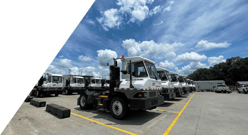 Fleet of yard trucks parked at industrial facility under blue sky